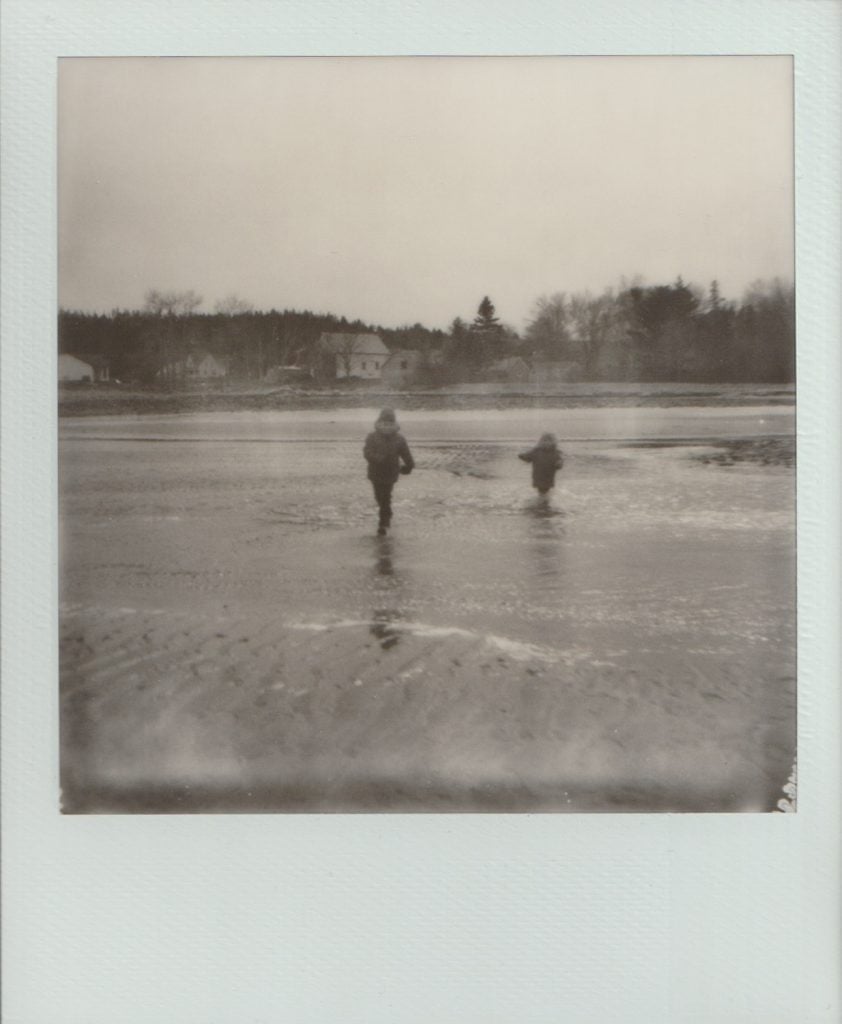 Polaroid film of two boys running through the water on a beach.
