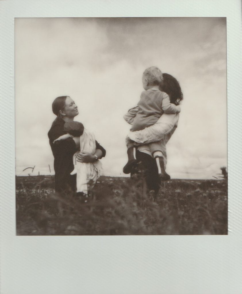 A mother and father look at each each tenderly as they hold their children. Shot on black and white polaroid film.