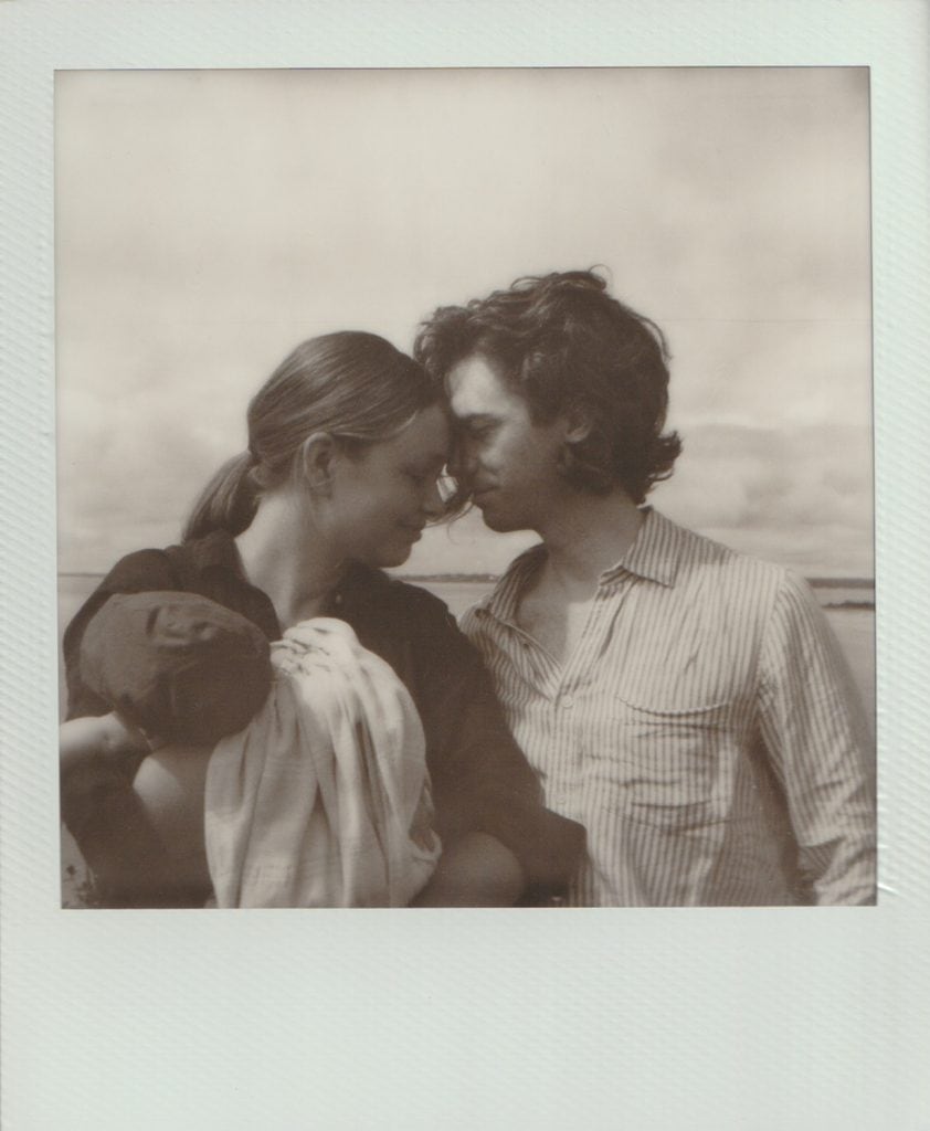 An SX 70 Black and White polaroid film of a mother and father holding their baby with their heads nestled together.
