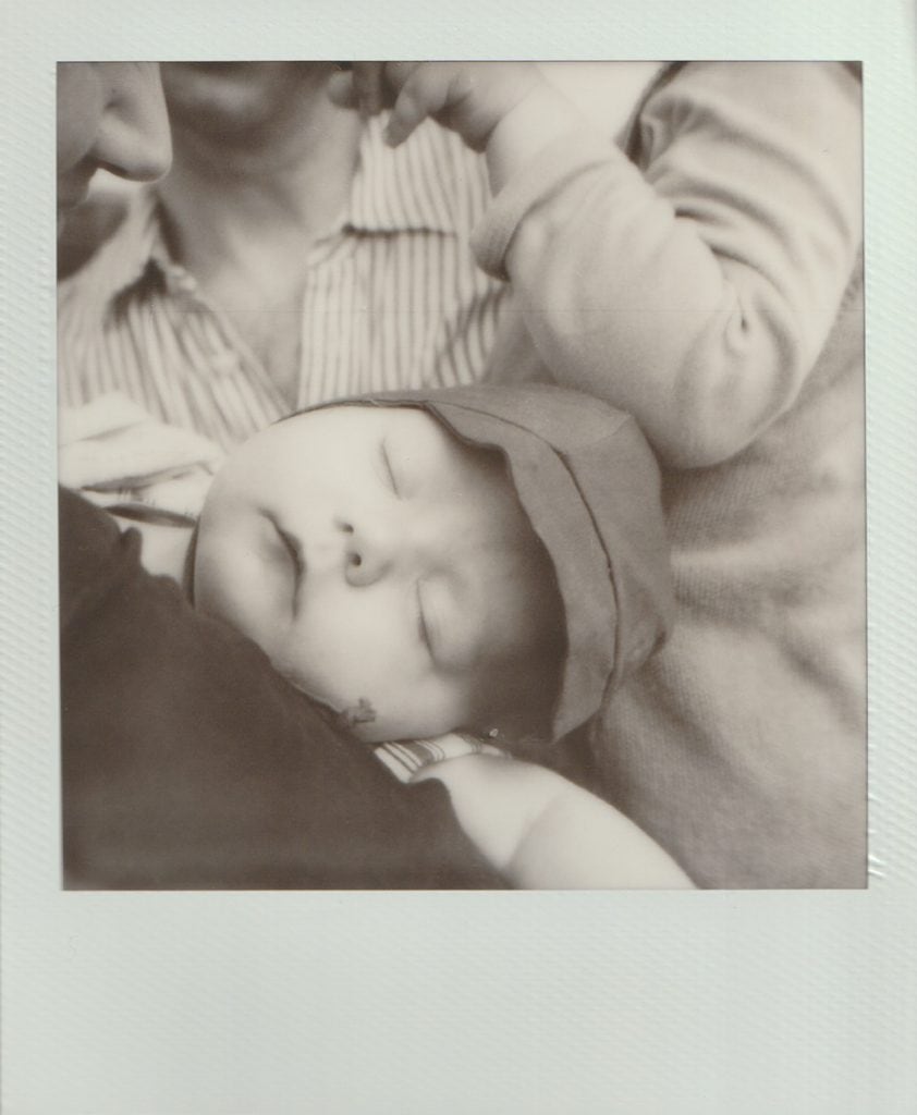 A sleeping baby is held by their mother on polaroid film.