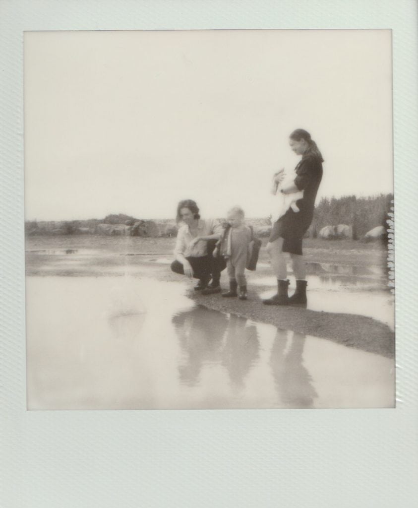 Polaroid film of a family throwing stones into a large puddle.