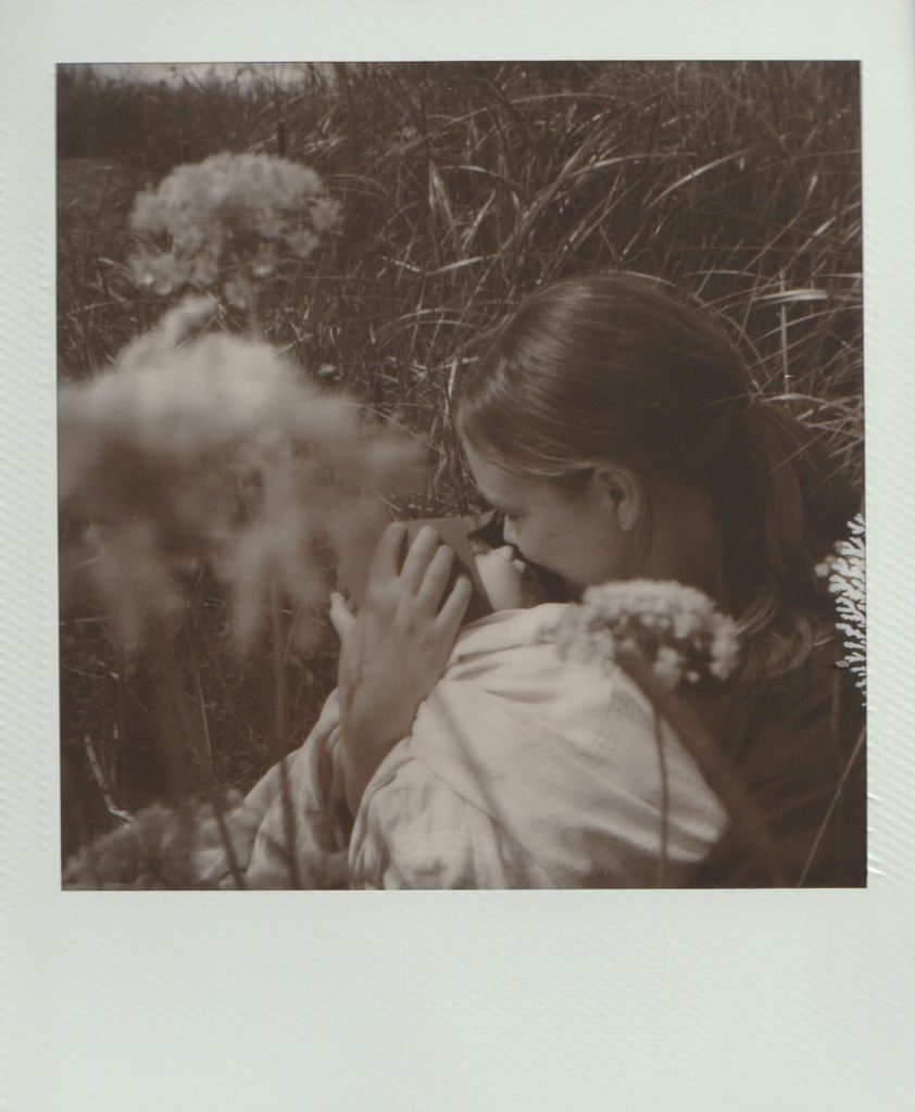 Polaroid film of a mother kissing her newborn baby in a field of flowers.