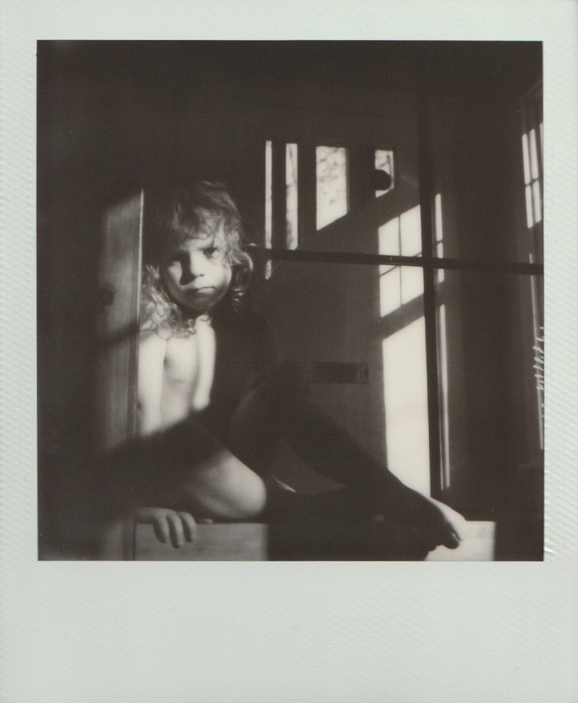 A little boy sitting in a pocket of light on polaroid film.