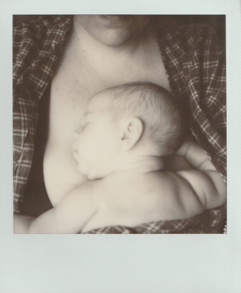Black and white Polaroid film of a newborn baby sleeping on their mother's chest.