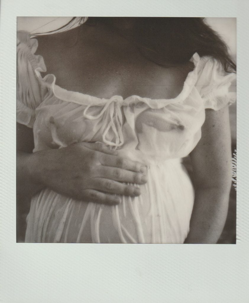 Vintage polaroid film of a maternity photograph. A woman holds her belly, wearing a see-through white dress.