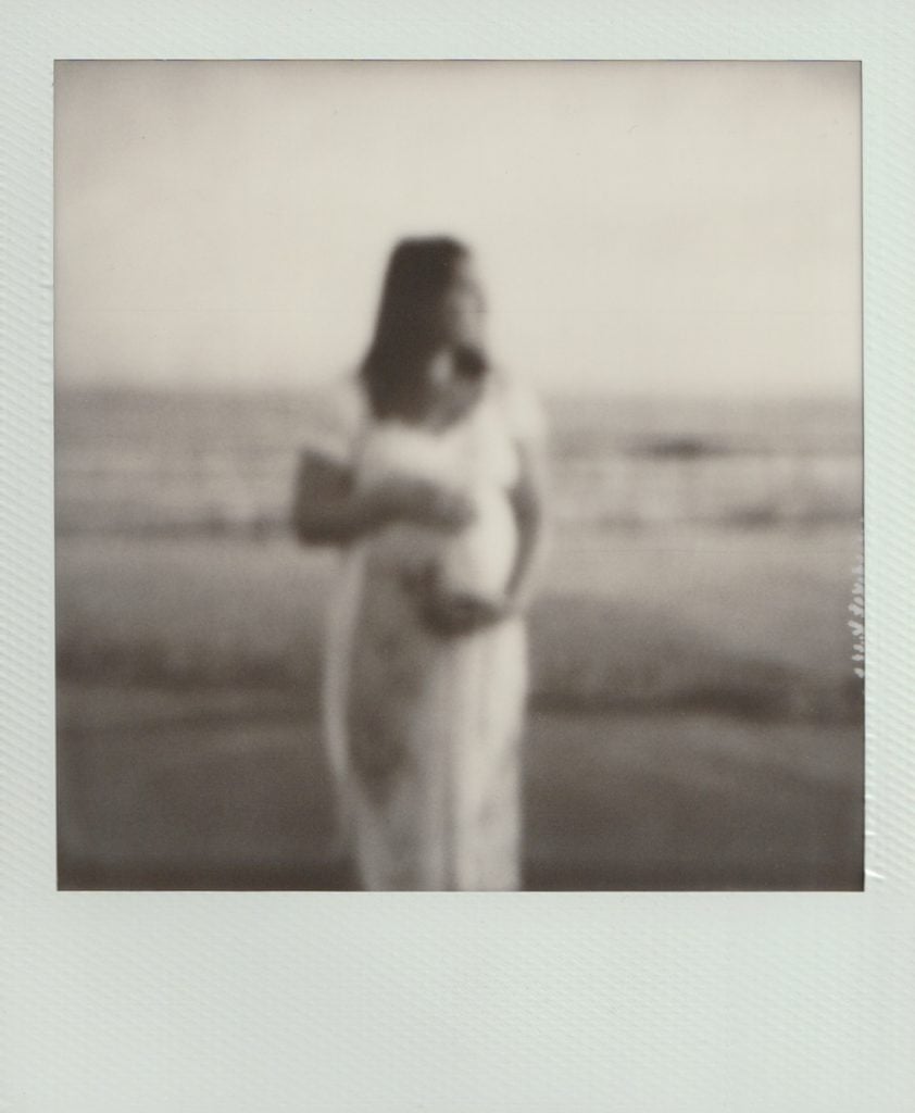 Polaroid film maternity session of a woman in a white dress holding her stomach.