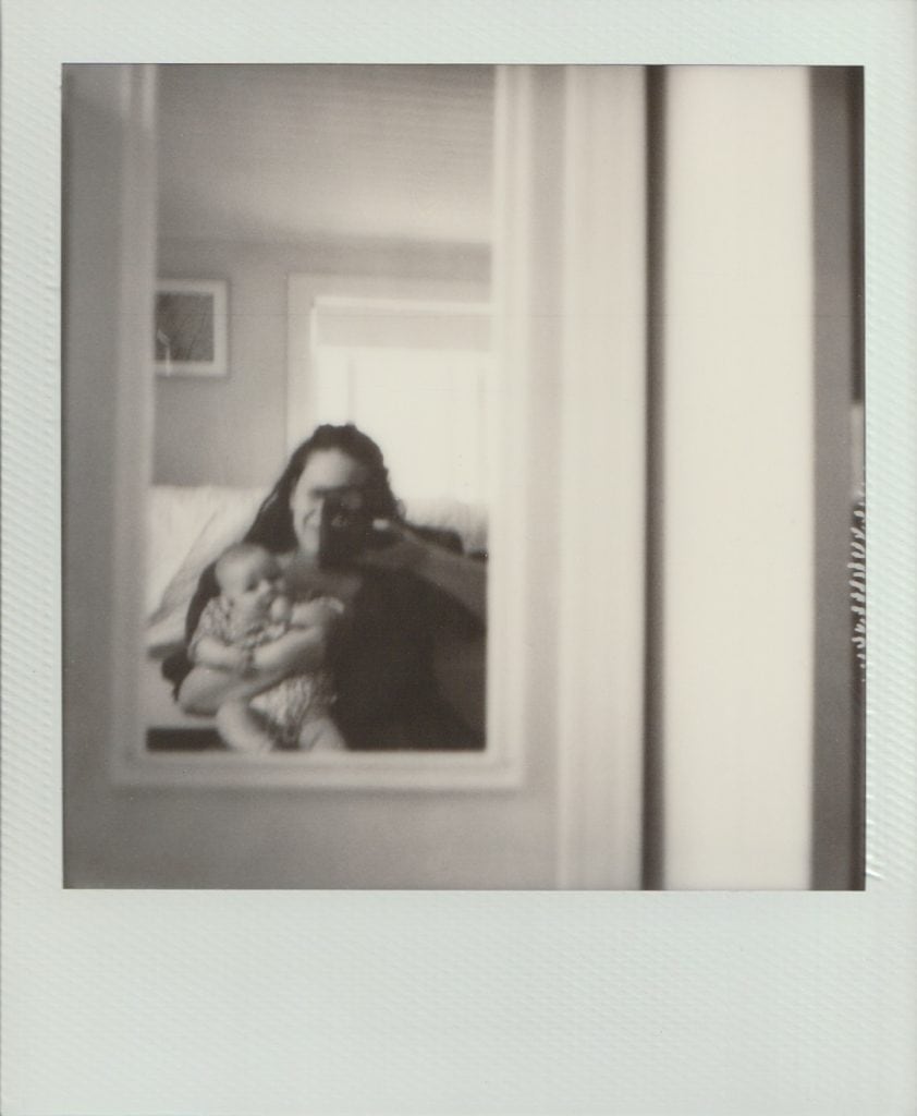A self portrait on polaroid of a mother holding her baby and taking a photograph in a mirror.
