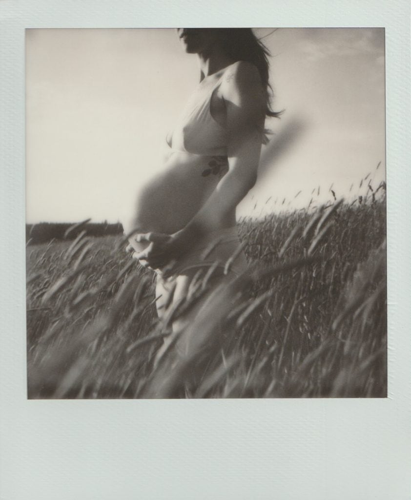 Polaroid film of a pregnant mother holding her belly in a field of tall grass.