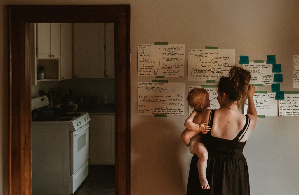 A faceless self portrait of Hanna Wolf holding her son and studying notes on the wall for her Canadian citizenship test.